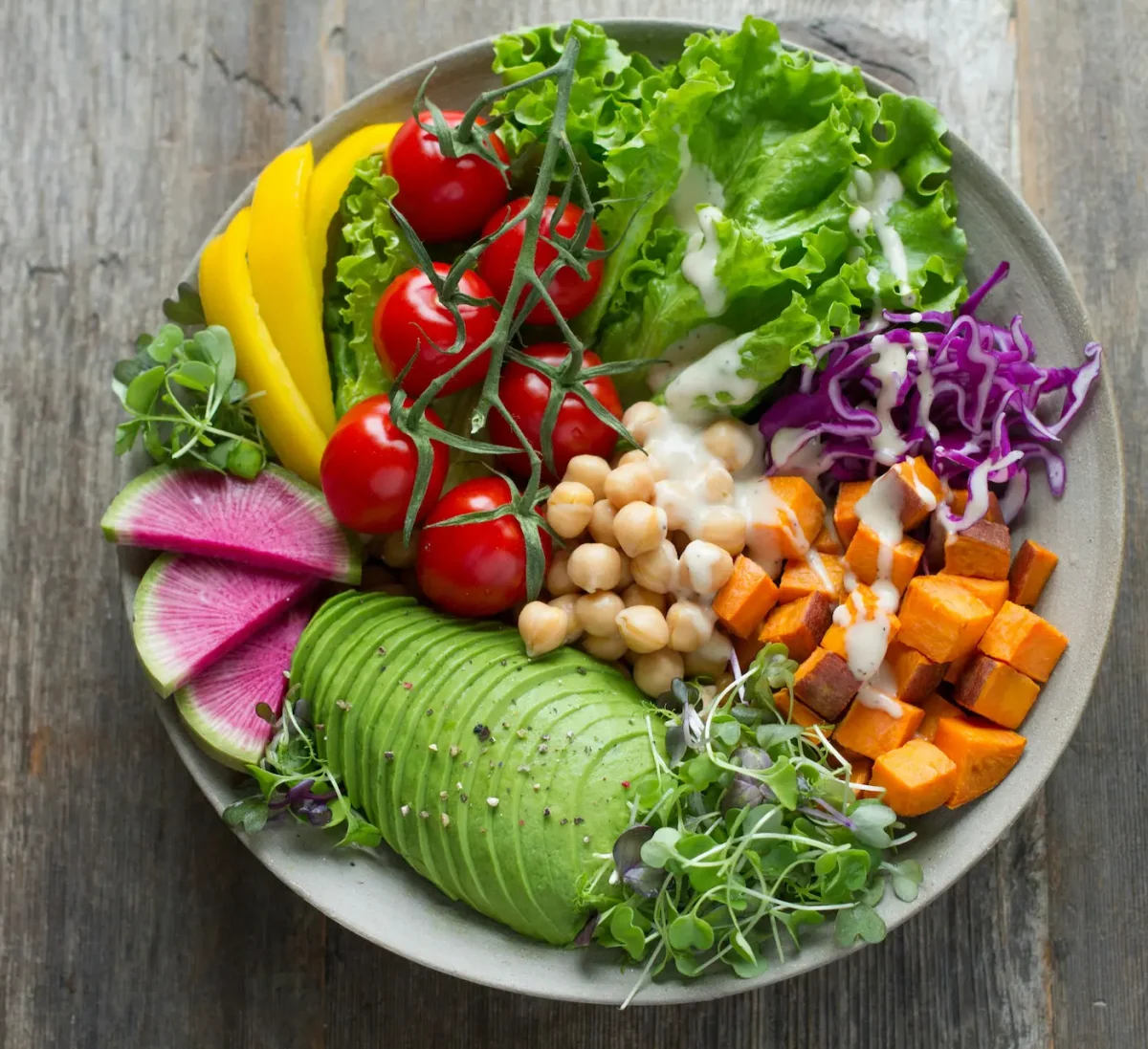 Bol de salade composée colorée avec avocat, pois chiches, patate douce, crudités et sauce
